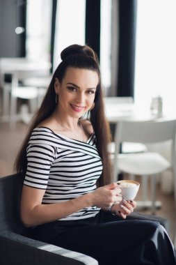 Bir fincan kahve ya da kapuçino pencere tutarak mükemmel bir gülümseme ile bir kadın portresi. Yetişkin Bayan bir kafede oturan ve çay içme.