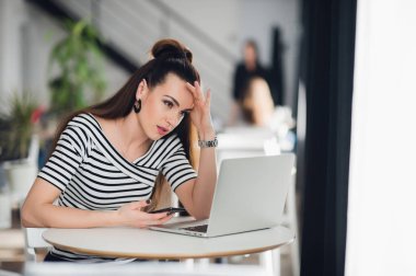 Endişeli ve üzgün bir kadın onun akrabalarından bir kafede kötü haberlerim var. Kadın bir laptop arıyorum ve telefon tutarak şaşkın.
