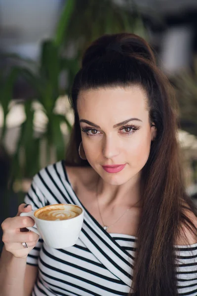 Retrato de cerca de una mujer en un café sosteniendo una taza de café o capuchino . — Foto de Stock