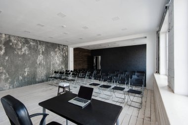 Oda bir sürü karanlık sandalye ile ders için. Duvarlar beyaz, çatı katı iç. Sağ tarafta bir kapı var. Arka plan üzerinde bir tablo ile bir dizüstü bilgisayar var.