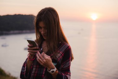 Gündoğumu veya günbatımı denize yakın cep telefonu kullanan kız.