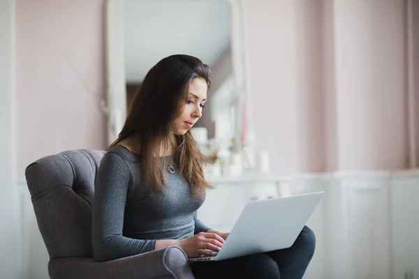 Mujer joven en moderno apartamento de lujo, sentada cómoda en sillón sosteniendo el ordenador en sus vueltas, relajante, trabajando en casa. autor del libro electrónico, soporte técnico remoto. Estilo de vida — Foto de Stock