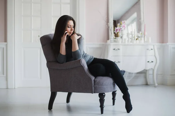 Fotografía de una mujer casual hablando con alguien en su teléfono móvil mientras está sentada en un sillón en casa . —  Fotos de Stock