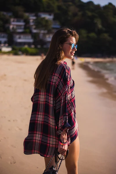 Летний образ жизни портрет молодой красивой девушки со спортивным загорелым телом, прогулка к пляжу тропического острова. Носит клетчатую футболку и стильные солнечные очки. С маленькой пляжной сумкой — стоковое фото
