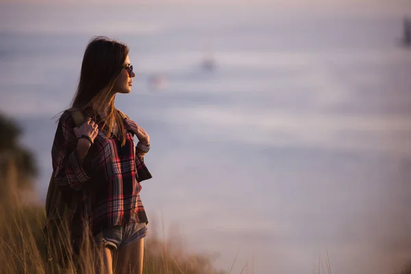 Mulher viajante olha para a borda do penhasco na baía do mar de montanhas no fundo ao pôr do sol — Fotografia de Stock