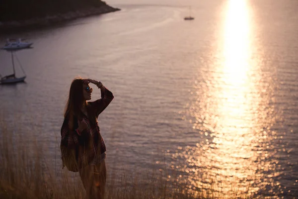 Женщина путешественник смотрит на край скалы на море бухте гор на заднем плане на закате — стоковое фото
