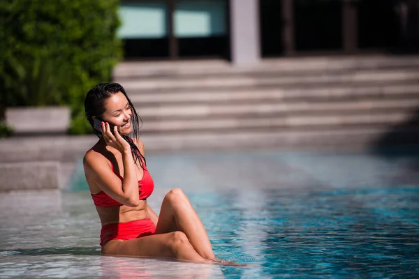 Mujer atractiva hablando en su teléfono móvil junto a la piscina — Foto de Stock