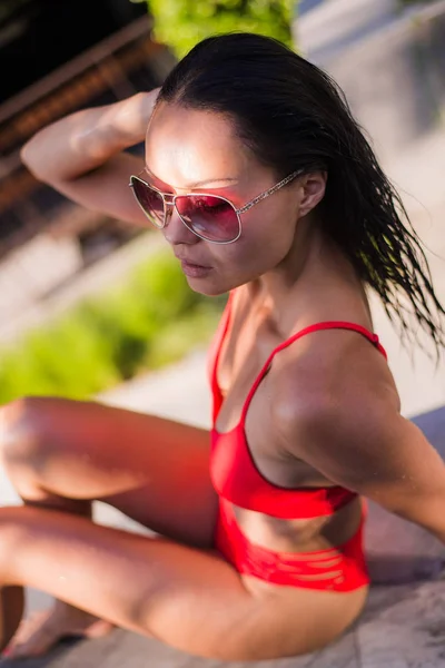 Close-up zomer portret van vrouw heerlijk ontspannen in het zwembad. Mooie brunette haar sexy vrouw meisje model in zonnebrillen en elegante rode sexy badpak lingerie met rond het zwembad — Stockfoto