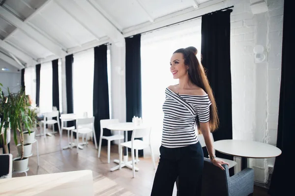 Hermosa hembra con linda sonrisa mirando hacia otro lado mientras se relaja después del trabajo. Encantadora mujer feliz disfrutando del descanso y buen día mientras se sienta sola en el interior de la cafetería moderna . — Foto de Stock