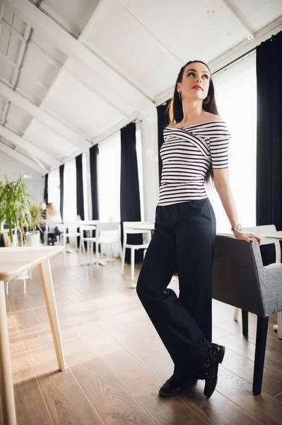 Portrait de belle jeune femme debout dans un café appuyé sur une chaise et regardant loin en souriant. Propriétaire de café femme réussie relaxant de son travail . — Photo