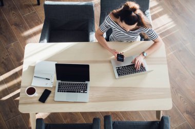 Üstten Görünüm onu laptop bir kafede kullanarak kadın. Bir fincan kahve ve cep telefonu dizüstü bilgisayarında net sörf ile bir masada oturan genç kadın havai çekim.