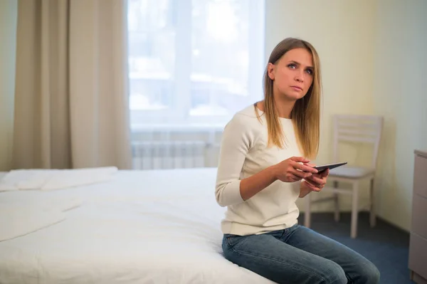 Joven mujer sonriente sentada en la cama en casa y conectándose con una tableta, relajarse y concepto de ocio — Foto de Stock