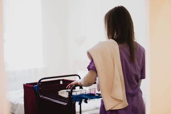Joven doncella empujando carro mientras limpieza habitaciones de hotel —  Fotos de Stock