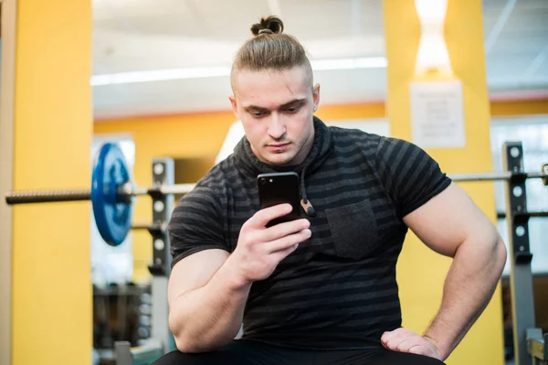 Молодой красивый мужчина, пользующийся телефоном во время перерыва в спортзале . — стоковое фото