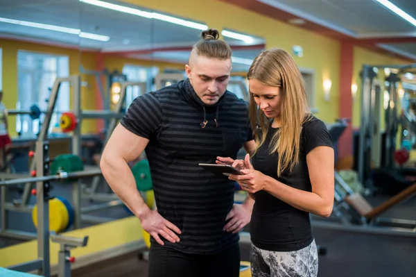 Adatto attraente giovane coppia in una palestra guardando un tablet-pc come monitorare i loro progressi e fitness — Foto Stock