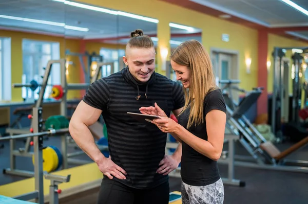 Fit attractive young couple at a gym looking at a tablet-pc as they monitor their progress and fitness