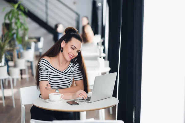 Imagen de la mujer feliz usando el ordenador portátil mientras está sentado en la cafetería. Mujer joven sentada en un café y hablando con amigos a través de Internet . —  Fotos de Stock