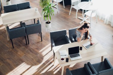 Havai görünümü olan bir masada oturan ve onu laptop çalışma çekici bir kadın. Ahşap zemin üzerinde grafik gölgeler güneş çevirir.