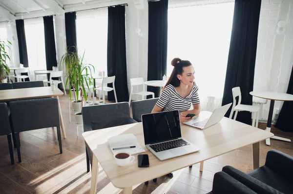 Portret van een doordachte vrouw achter een laptop in een cafe zit en op zoek weg. — Stockfoto