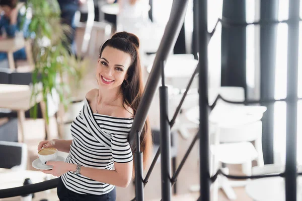 Mujer joven adulta, hermosa y natural en un café. Sonriente y atractiva hembra de pie en interiores . — Foto de Stock