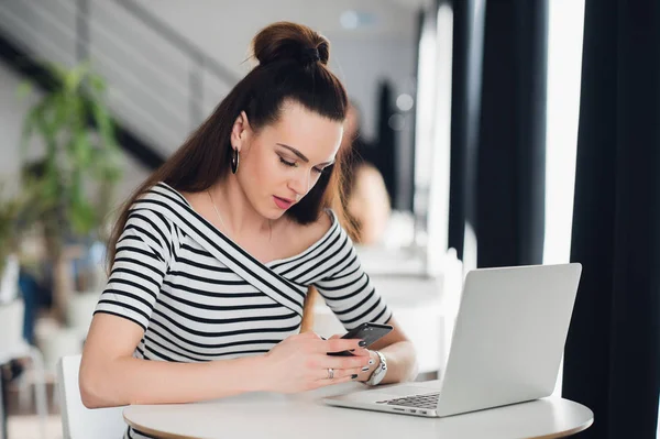 Adulto atraente mulher sonolenta em seu trabalho segurando telefone e sentado com um laptop. Menina bonita cochilando no trabalho . — Fotografia de Stock