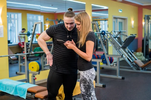 Fitness, sport, attività fisica, tecnologia e dieta - giovane donna sorridente e personal trainer con smartphone in palestra — Foto Stock