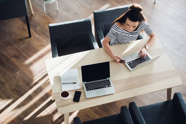 Vrouw van de multitasking in een café, die werkt op zowel telefoon en laptop, terwijl haar collega rust. — Stockfoto