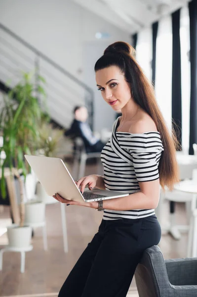 Piękna kobieta dorosłych trzyma laptopa i patrząc na kamery, stojąc w kafejce pusty. — Zdjęcie stockowe