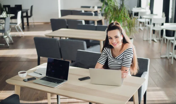 Mulher adulta com um sorriso perfeito sentada em um café com um laptop, segurando uma xícara de café e olhando para a câmera . — Fotografia de Stock