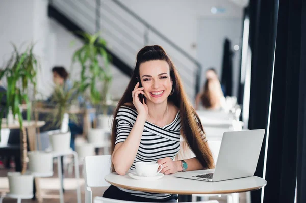 Executive kobieta uśmiechając się i pracuje w trybie online z laptopa podczas rozmowy na telefon w kawiarni. — Zdjęcie stockowe