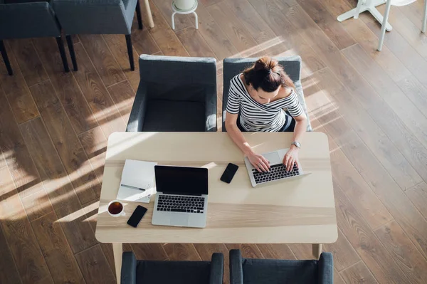 Visão superior da mulher adulta ocupada preparando seu trabalho para o prazo. Fotografia aérea de uma mulher atraente sentada em um café com um laptop e telefone . — Fotografia de Stock