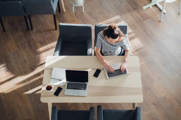 Bovenaanzicht van drukke volwassen vrouw voorbereiding van haar werkzaamheden voor de deadline. Overhead schot van een aantrekkelijke vrouw zitten in een cafe met een laptop en telefoon. — Stockfoto