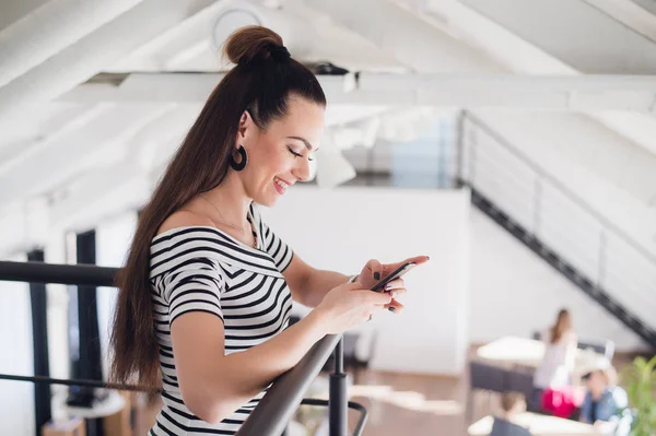 Joven empresaria está de pie en la cafetería y comprobar los mensajes en el teléfono inteligente. Chica está esperando a amigos, colegas en el restaurante . — Foto de Stock