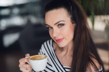 Bir fincan kapuçino tutarak ve kameraya arıyorsunuz büyüleyici bir kadın portresi yakın çekim.