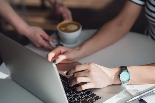 Close-up foto van handen van een ober geven een kopje cappuccino aan een vrouw te typen met een toetsenbord. — Stockfoto