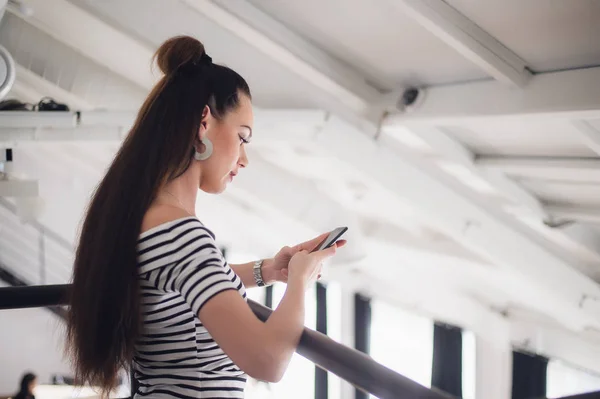 Enviando mensajes de texto a una mujer sentada en la mesa y sosteniendo el teléfono móvil, pensando. Mujer adulta sentada con un portátil y mirando hacia otro lado . — Foto de Stock