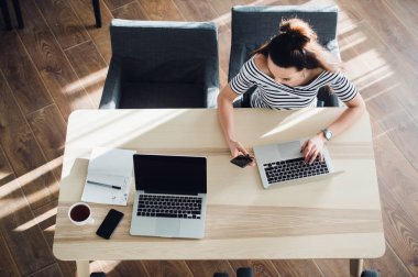 Genç kadın manifatura cep telefonu ve masasında otururken notlar yazma ile meşgul. Çok beyaz kadın ev ofis veya bir kafe onu laptop ile çalışma.