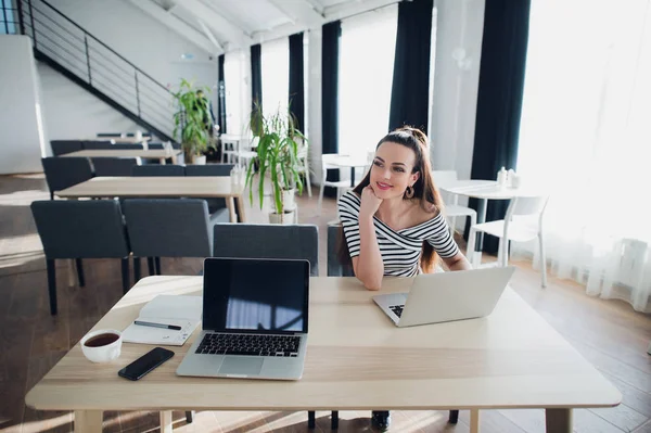 Doordachte mooie vrouw met een stille glimlach zitten werking voort te laptop in een café op zoek pensively weg met haar kin op haar hand. — Stockfoto