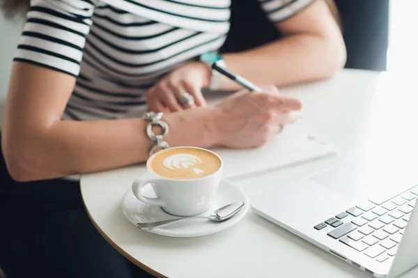 Um caderno em branco branco com uma caneta de luxo e uma xícara de café Latte com laptop borrado no fundo . — Fotografia de Stock