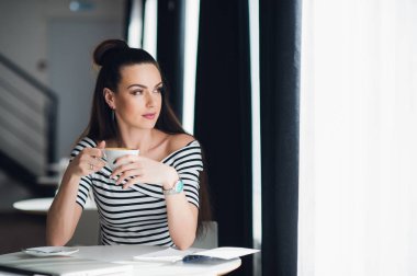 Çekici yetişkin kadın bir kafede oturan ve bir pencere birini, bir fincan sıcak kahve tutarken rüya yoluyla bakan.