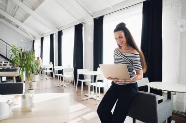 Güzel esmer kadın ayakta ve kameraya bakarken onu laptop holding.