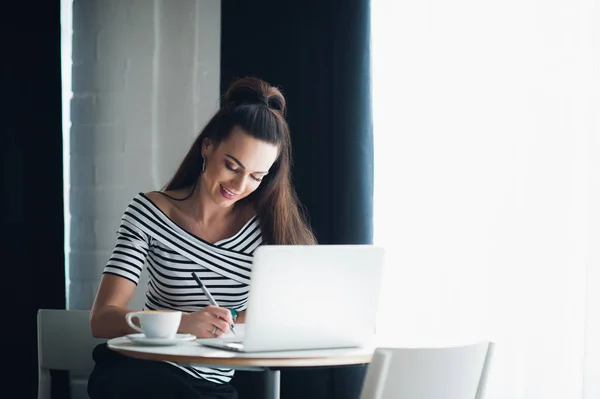 Atractiva joven escribiendo en su cuaderno y tomando café en un café . — Foto de Stock