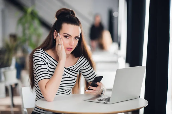 Mujer con expresión seria llena de conmoción y perplejidad sostiene un teléfono inteligente mientras mira a la cámara . — Foto de Stock