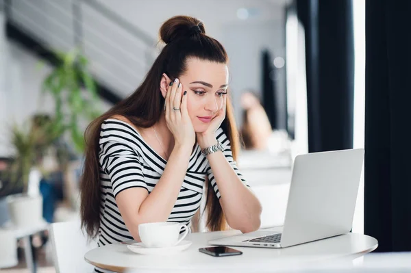 Gelangweilte junge Frau im Büro, die mit einem Laptop arbeitet und auf den Computerbildschirm starrt. — Stockfoto