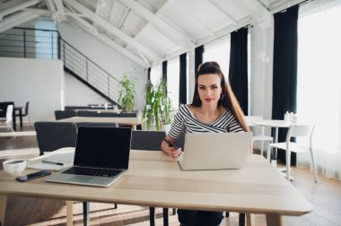 Dizüstü bilgisayar telefonla sohbet kullanırken coworking ofiste oturan genç neşeli Bayan fotoğrafı. Kameraya bakarak.