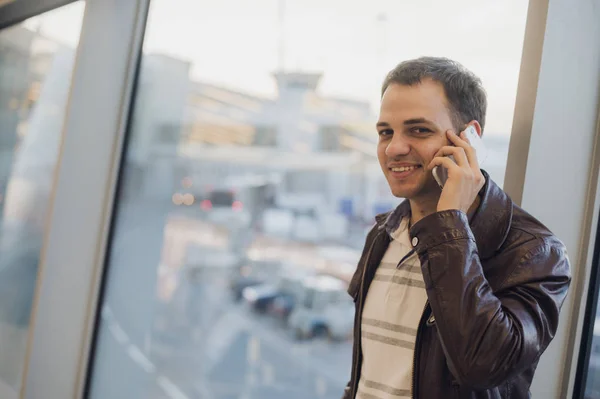 Jeune voyageur à l'aéroport, veste en cuir sur son smartphone — Photo