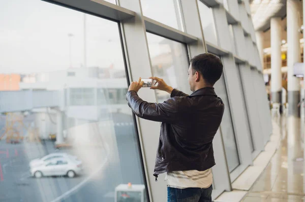 Viajero con teléfono móvil en el aeropuerto tomando fotos de su avión. Instalaciones de control del tráfico aéreo en segundo plano —  Fotos de Stock