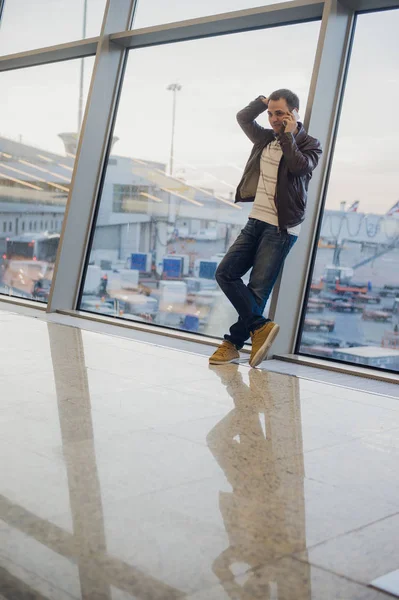 Kommer att bli hem snart. Porträtt av en stilig ung man skrattar talar på telefonen medan du väntar hans flyg på flygplatslounge — Stockfoto