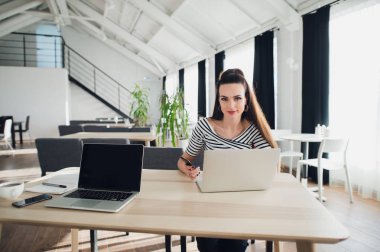 Yeni fikirler bir tasarımcı çalışma eve portresi. Koyu saç örgülü kadın rahat kıyafetler beyaz bir masada oturuyor, o kameraya, onun önünde bir dizüstü bilgisayar ile bir kalem tutan bakıyor.