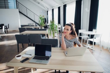 Genç çekici kadın ile bir dizüstü bilgisayar masada oturan ve Yardımcısı yokken telefon, holding.